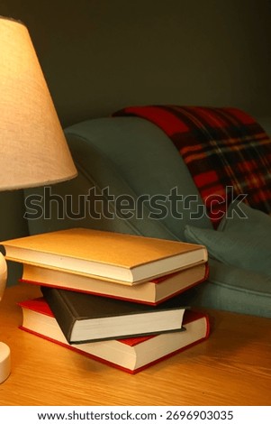 Stack of books next to a cozy couch and warm lamp light, creating a relaxing atmosphere for reading and knowledge