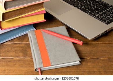 A stack of books, a notebook with a pen and a laptop on a wooden table. E-learning concept.