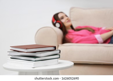 Stack of books on table at home and woman with headphones on background. Audiobook concept