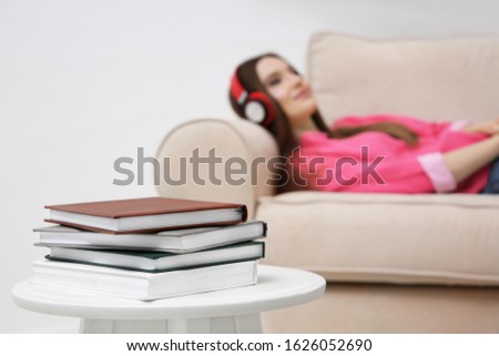 Stack of books on table at home and woman with headphones on background. Audiobook concept