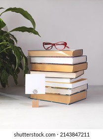 A stack of books on a white background. Glasses on the top book. World book day concept. Holder with empty card. Copy space.