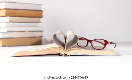 A stack of books on a white background. Glasses on the top book. World book day concept. Holder with empty card. Copy space.