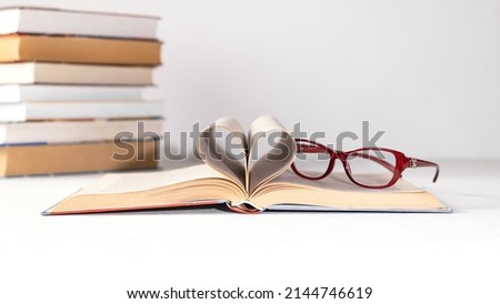 A stack of books on a white background. Glasses on the top book. World book day concept. Holder with empty card. Copy space.