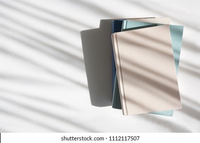 Stack Of Books On A White Table Next To A Window With Dappled Light