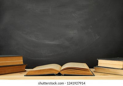 stack of books over wooden desk in front of blackboard