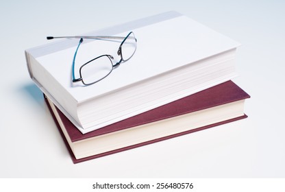 Stack of books and a pair of reading glasses on white background