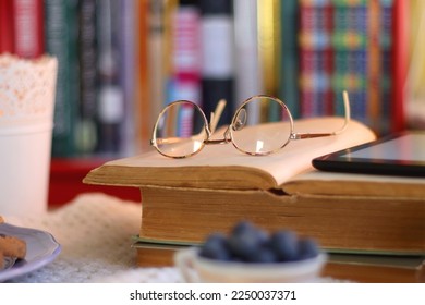 Stack of books, reading glasses and tablet on the table. Hygge at home. Selective focus.