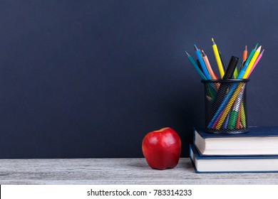 A stack of books, a red apple and colorful pencils in a case, on a dark background with a place for inscription.
