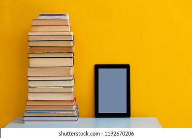 Stack of books versus kindle or tablet for reading, technology innovative education concept on yellow background, copy space