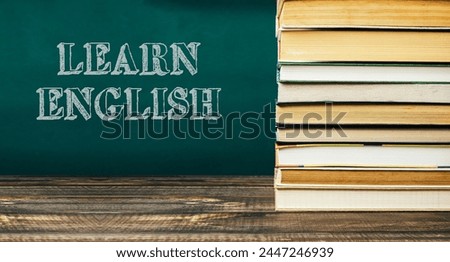 A stack of books with the word learn English written on a green chalkboard. The books are piled on top of each other, creating a sense of importance and emphasis on the subject