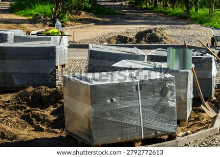 A stack of bricks wrapped in plastic sits on a pallet by the roadside.