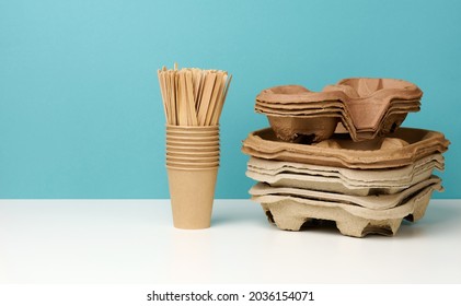 a stack of brown disposable paper cups and a stand on a white table, blue background. Utensils for takeaway drinks, zero waste