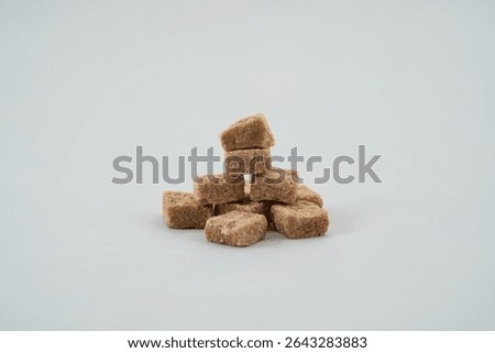 A stack of brown sugar cubes neatly arranged in a pyramid shape on a clean white background. The cubes showcase their rough texture and natural color.