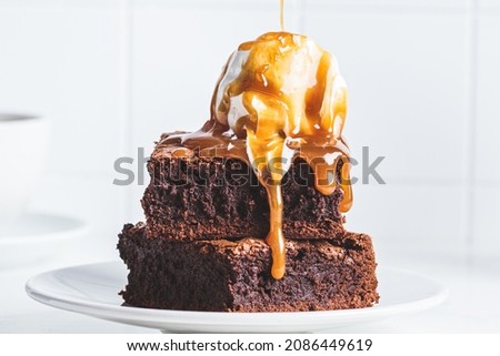 Stack of brownie squares with a scoop of ice cream and caramel, white background.
