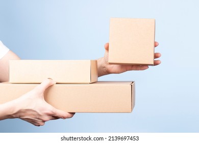 Stack of cardboard boxes in female hands. Woman showing small blank brown box. Blank parcel boxes on light blue background. Packaging, shopping, free shipping, delivery concept