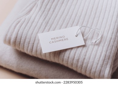 Stack of cashmere clothes with label, tag on beige background. Merino wool clothes. Set of wool organic baby clothes. Copy space.