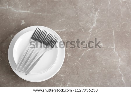 Stack of ceramic dishware with cutlery on grey background, top view