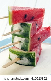 Stack of chilled watermelon with ice cream sticks on white wooden background.