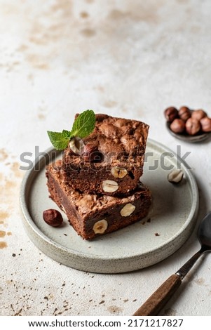 Stack of chocolate brownies with hazelnuts and mint leaf on a plate with spoon with text space. Vertical orientation
