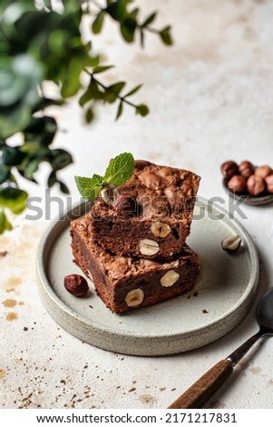 Stack of chocolate brownies with hazelnuts and mint leaf on a plate with spoon and greenery in blur with text space. Vertical orientation