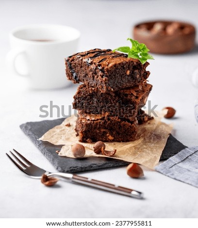 A stack of chocolate brownies with mint, hazelnuts and salted caramel on baking paper on a light background with a cup of coffee. The concept of delicious and sweet homemade baked goods for breakfast.