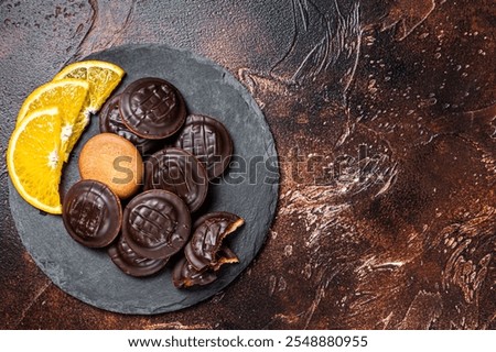 Stack of Chocolate Covered Round Jaffa Cookies with Orange Flavored Marmalade. Dark background. Top view. Copy space.