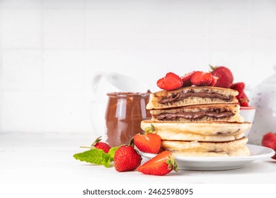 Stack of chocolate spread filled pancakes. Sweet breakfast pancakes with chocolate sauce inside it, and fresh stawberries, on white kitchen table