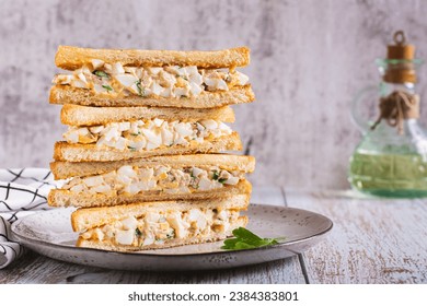 Stack of chopped egg, bacon and herb salad sandwiches on a plate