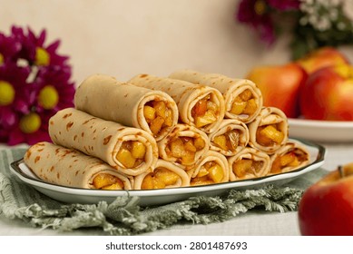 Stack of Cinnamon apple crepe roll served on a white plate. Fresh apples and autumn flowers on background.