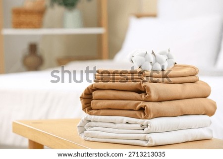 Stack of clean bed linen with cotton flowers on bench in bedroom, closeup