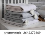 Stack of clean bed sheets with cotton flowers on table near grey brick wall in room