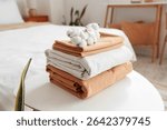 Stack of clean bed sheets with cotton flowers sprig on table in bedroom