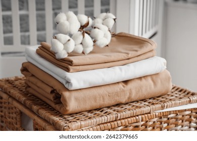 Stack of clean bed sheets with cotton flowers sprig on wicker laundry basket in room