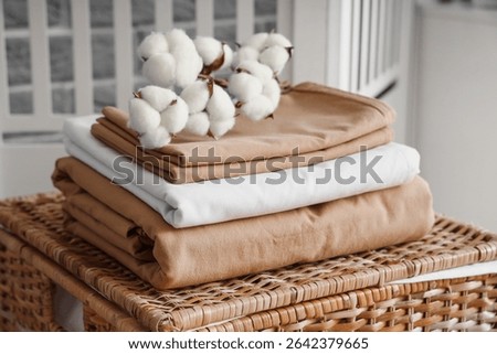 Stack of clean bed sheets with cotton flowers sprig on wicker laundry basket in room