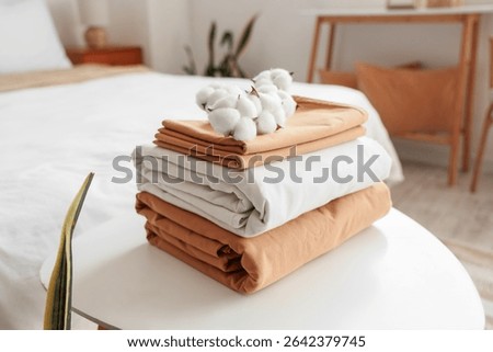 Stack of clean bed sheets with cotton flowers sprig on table in bedroom