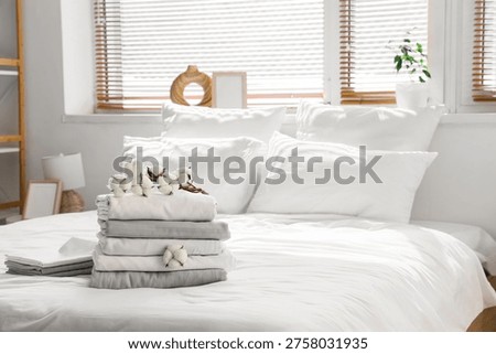Stack of clean bed sheets with cotton flowers in bedroom