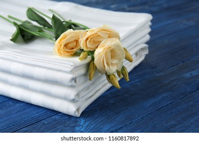 Stack Of Clean Bed Sheets And Flowers On Color Wooden Background