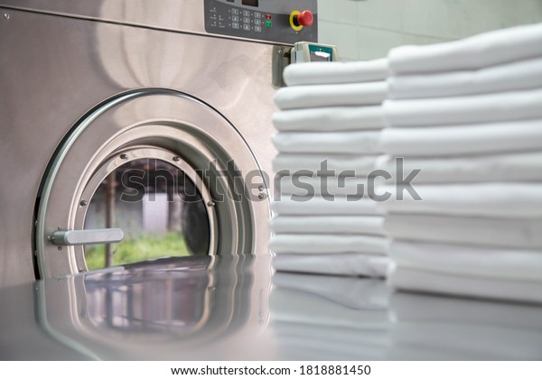 Stack
of clean bed sheets in front of industrial washing machine. Focused
on washing machines. 
Shot taken in the
factory.
