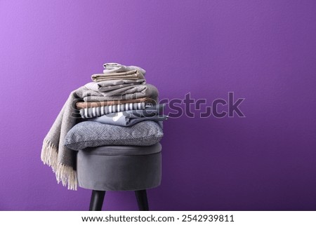 Stack of clean bed sheets and pillow on stool against purple background. Space for text