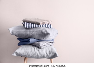 Stack of clean bed sheets and pillows on stool near beige wall. Space for text
