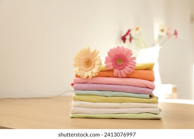 Stack of clean clothes and flowers on wooden table. Space for text