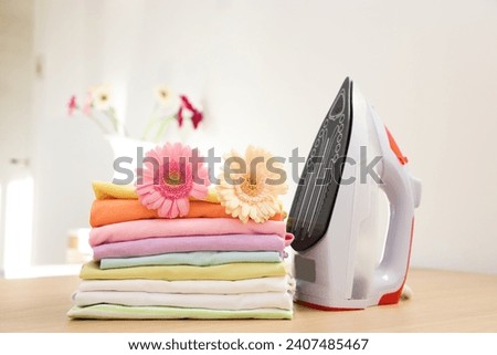 Stack of clean clothes, modern iron and flowers on wooden table