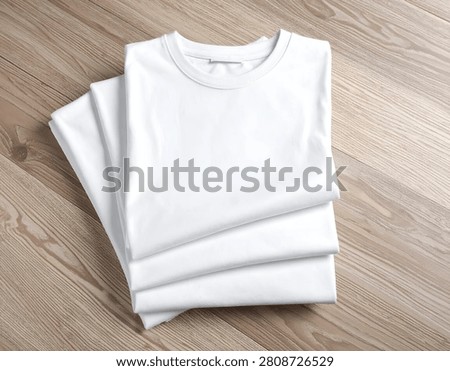 Stack of clean, folded white shirts on a light wood surface, overhead shot