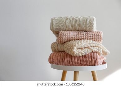 Stack of clean freshly laundered, neatly folded women's clothes on wooden table. Pile of shirts, dresses and sweaters on the table, white wall background. Copy space, close up, top view. - Shutterstock ID 1836252643