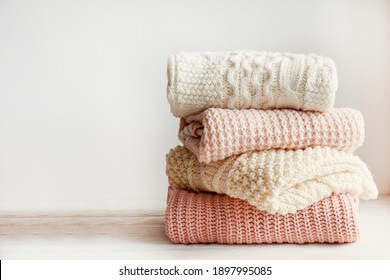 Stack Of Clean Freshly Laundered, Neatly Folded Women's Clothes On Wooden Table. Pile Of Shirts And Sweaters On The Table, White Wall Background. Copy Space, Close Up, Top View.