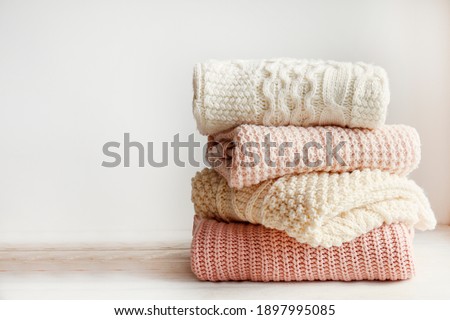 Stack of clean freshly laundered, neatly folded women's clothes on wooden table. Pile of shirts and sweaters on the table, white wall background. Copy space, close up, top view.