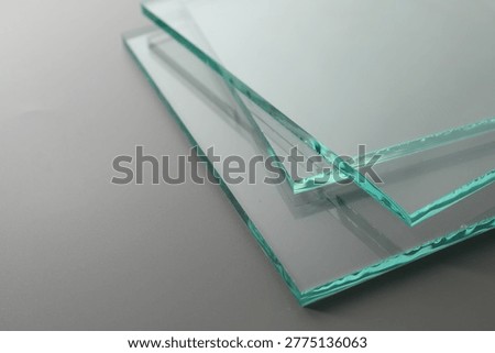 Stack of clean glass sheets on grey background, closeup. Space for text