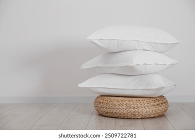 Stack of clean pillows on wicker pouf near white wall. Space for text