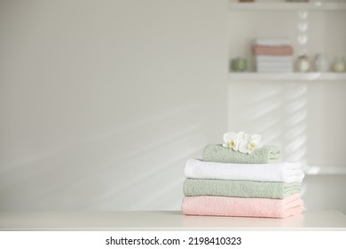 Stack of clean soft towels with orchid flowers on white table indoors. Space for text
