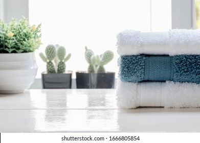 Stack Of Clean Towels And Houseplant On White Wooden Table Near Window Sill, Bright Light Background And Copy Space.